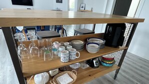 Una mesa de madera con estantes que sostienen diferentes utensilios de cocina, como cristalería, platos y tazas.