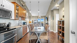 A modern kitchen with stainless steel appliances, a dining area with wicker chairs, and a view to the outside.