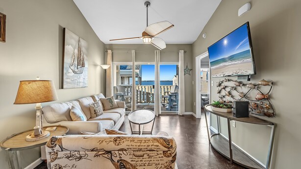 A living room with a sofa, a coffee table, a TV, and a balcony with a view of the ocean.