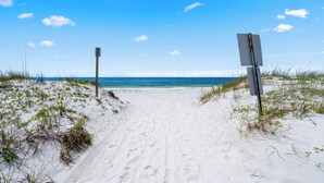 A sandy beach path leading to the ocean with a clear sky.