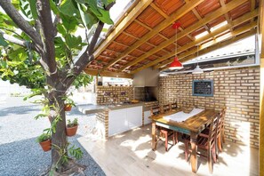 An outdoor dining area with a brick wall, wooden ceiling, and a tree with potted plants.