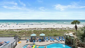 A pool area with lounge chairs and umbrellas, overlooking a beach with the ocean in the background.