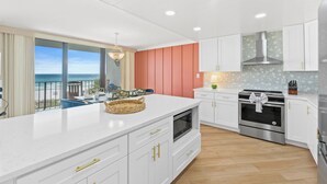 A modern kitchen with white cabinetry, a large island, and a view of the ocean.