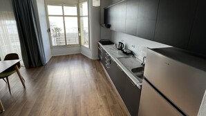 A modern kitchen with dark cabinets, a stainless steel refrigerator, and a large window with a view of the beach. - Wave Beachfront Apartments (Durrës)