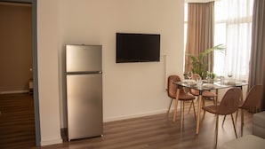 A modern living room with a dining area, a flat-screen TV mounted on the wall, and a built-in refrigerator. - Wave Beachfront Apartments (Durrës)