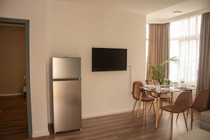 Una sala de estar moderna con comedor, un televisor de pantalla plana montado en la pared y un refrigerador empotrado.