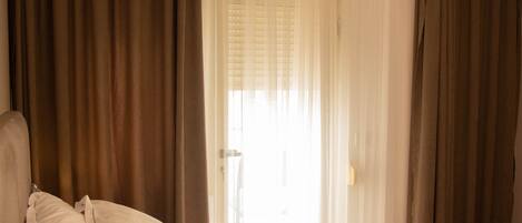 A hotel room with a bed, curtains, and a window with blinds.