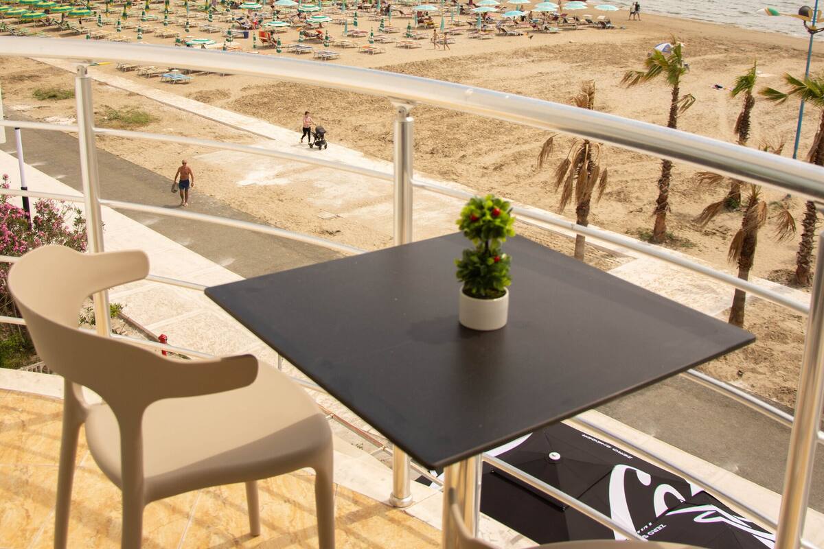 Ein Balkon mit Tisch und Stühlen mit Blick auf einen Strand, der mit Sonnenschirmen und Palmen belegt ist.