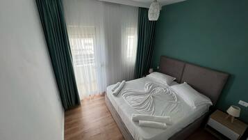 A modern hotel room with a large bed, a bedside table with a lamp, and sheer curtains allowing natural light.