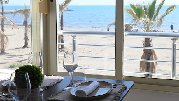 A dining table with a view of the beach and ocean through a window. - Wave Beachfront Apartments (Durrës)
