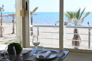 Una mesa de comedor con vista al mar y la playa a través de una ventana.