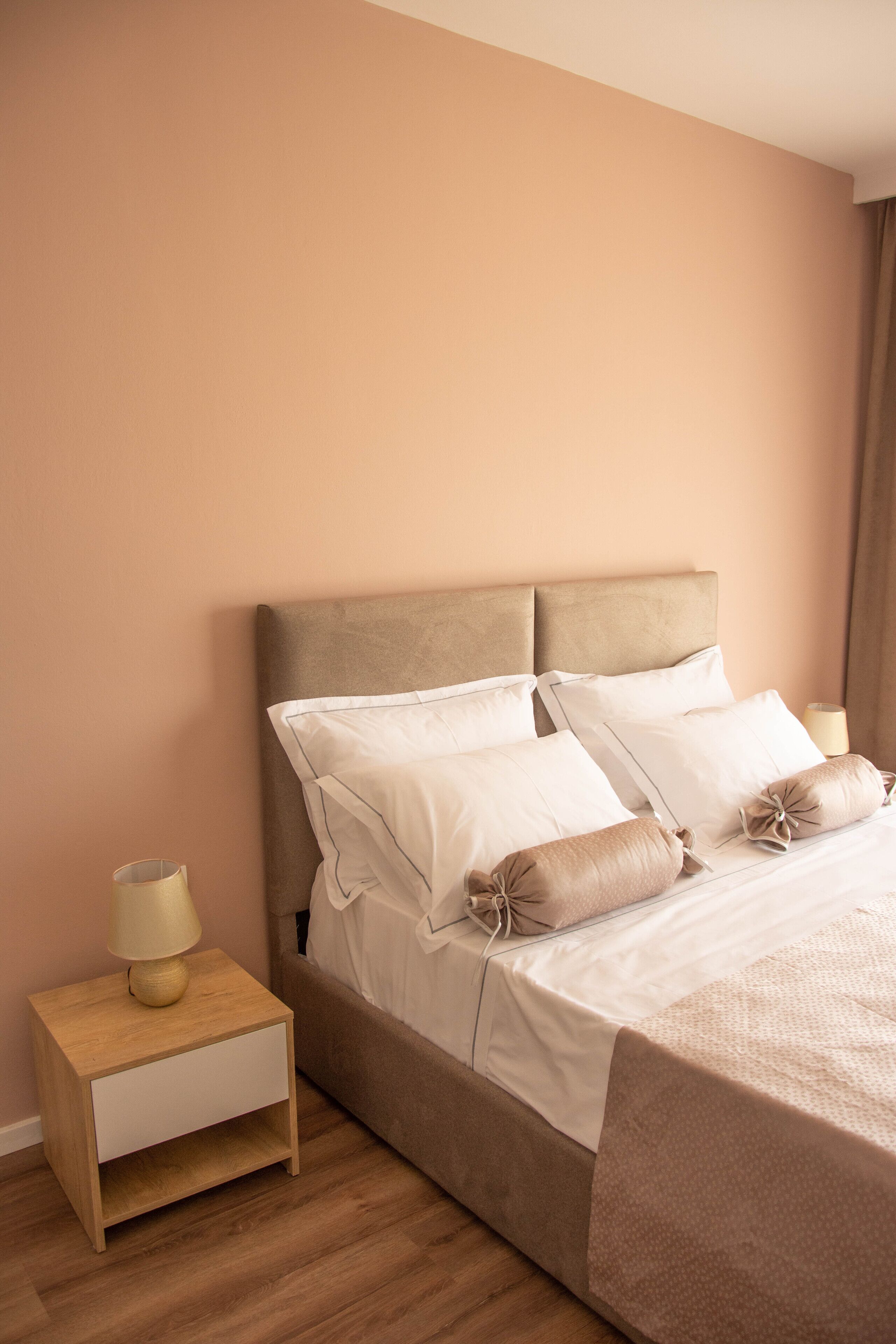 A neatly made bed with a headboard, a bedside table with a lamp, and a wooden floor.