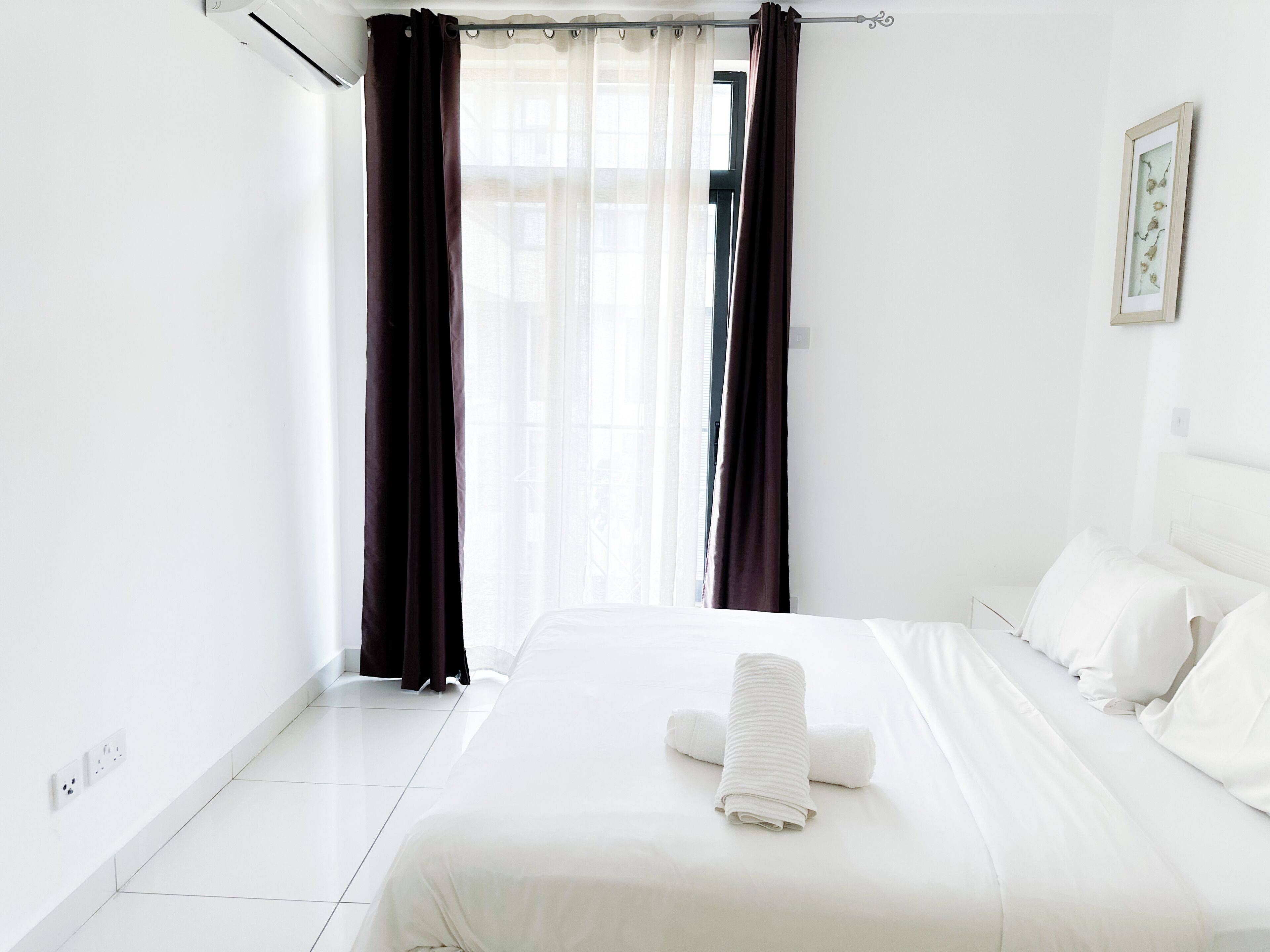 A hotel room with a large bed, white bedding, a rolled towel, and dark curtains.