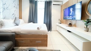A modern hotel room with a bed, a TV, a wooden console, and a potted plant.