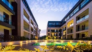 A modern hotel with a central courtyard featuring a swimming pool, surrounded by multi-story buildings with balconies and large windows.