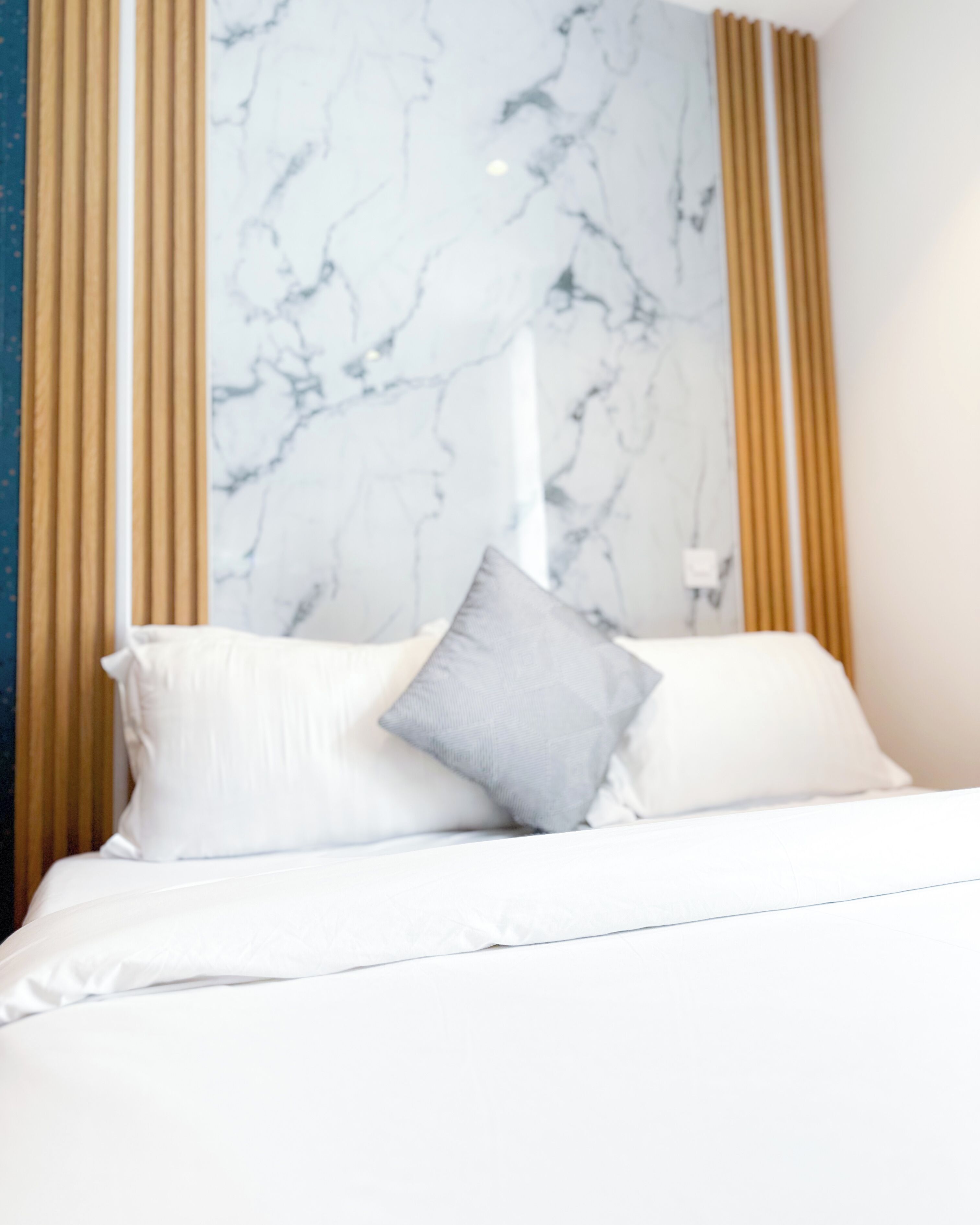 A bed with white bedding and a grey pillow, a marble wall, and curtains.