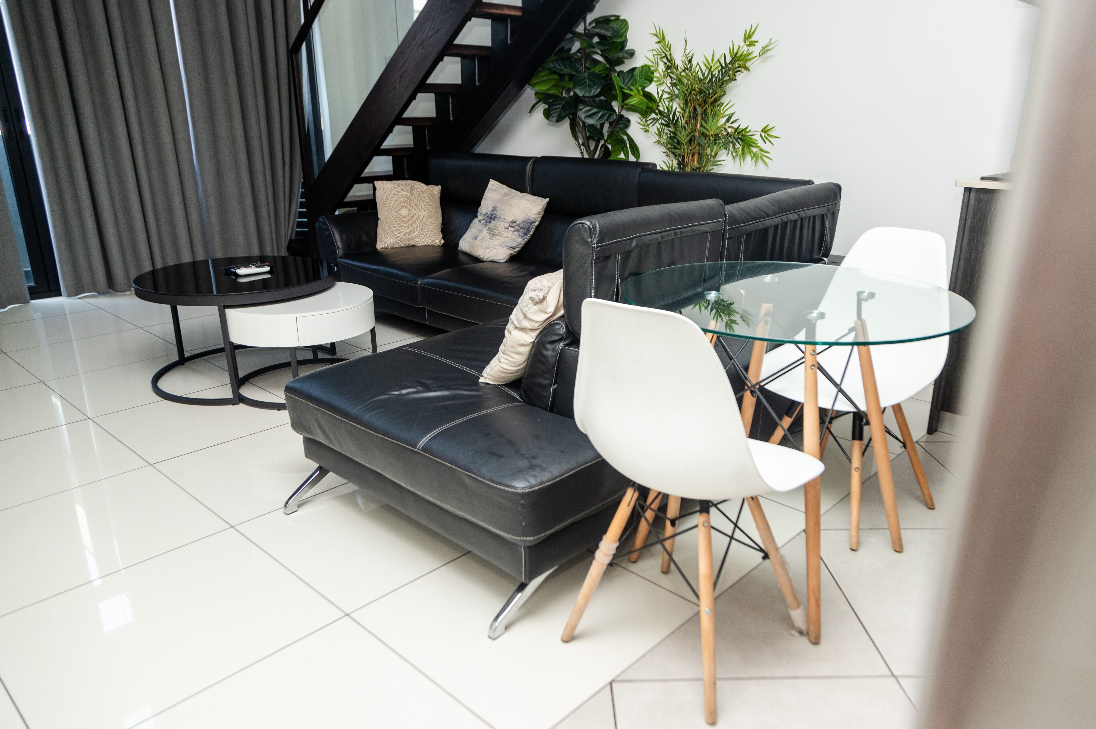 Una sala de estar moderna con un sofá de cuero negro, una mesa de centro de vidrio y sillas blancas.