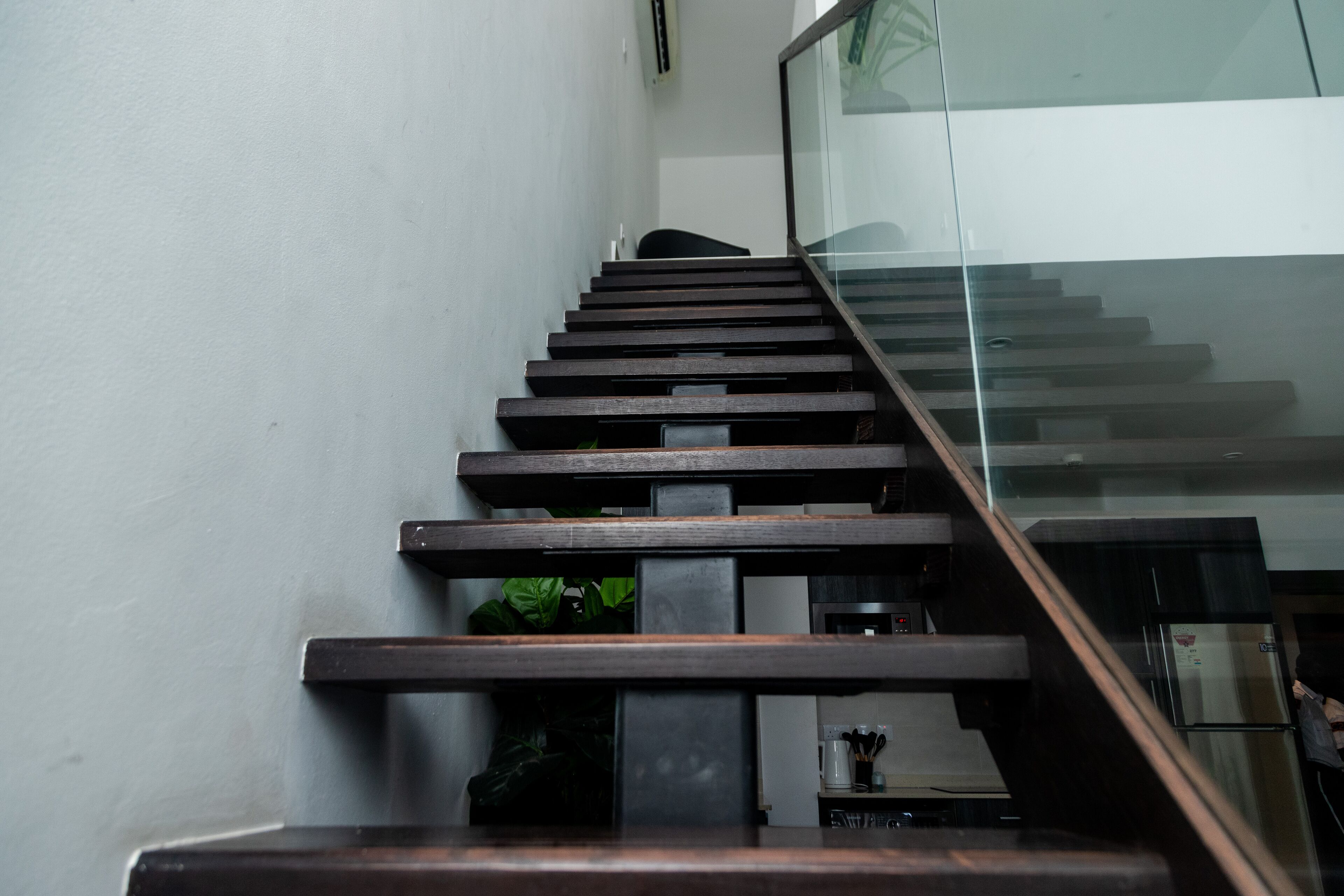 A modern staircase with wooden steps and glass railings, leading to a landing area with a kitchen appliance.