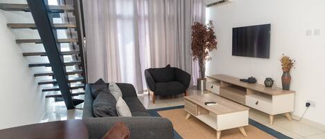 A modern living room with a sofa, a coffee table, a TV, and a staircase.