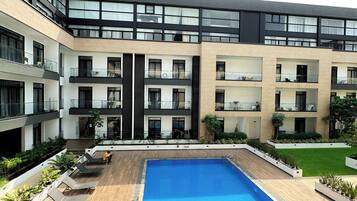 A modern building with a central swimming pool, multiple balconies, and a well-maintained garden area.