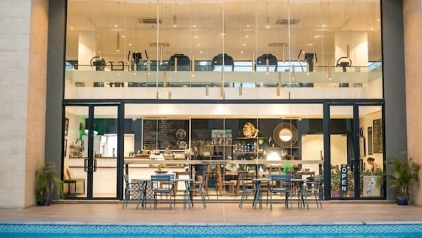A modern restaurant with a glass facade, outdoor seating, and a pool area.