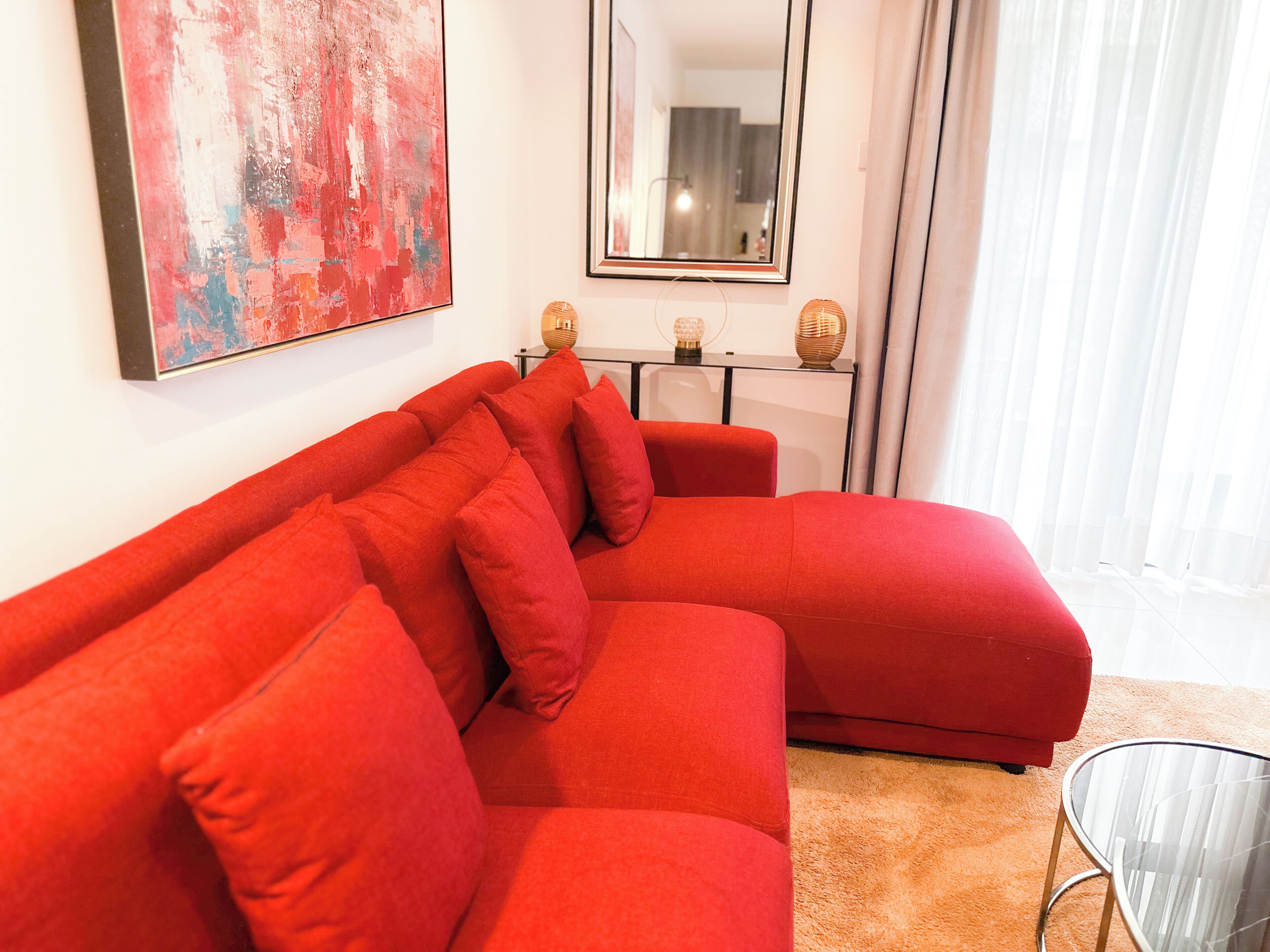 Una sala de estar moderna con un sofá seccional rojo, una mesa de centro de vidrio y un cuadro abstracto grande en la pared.