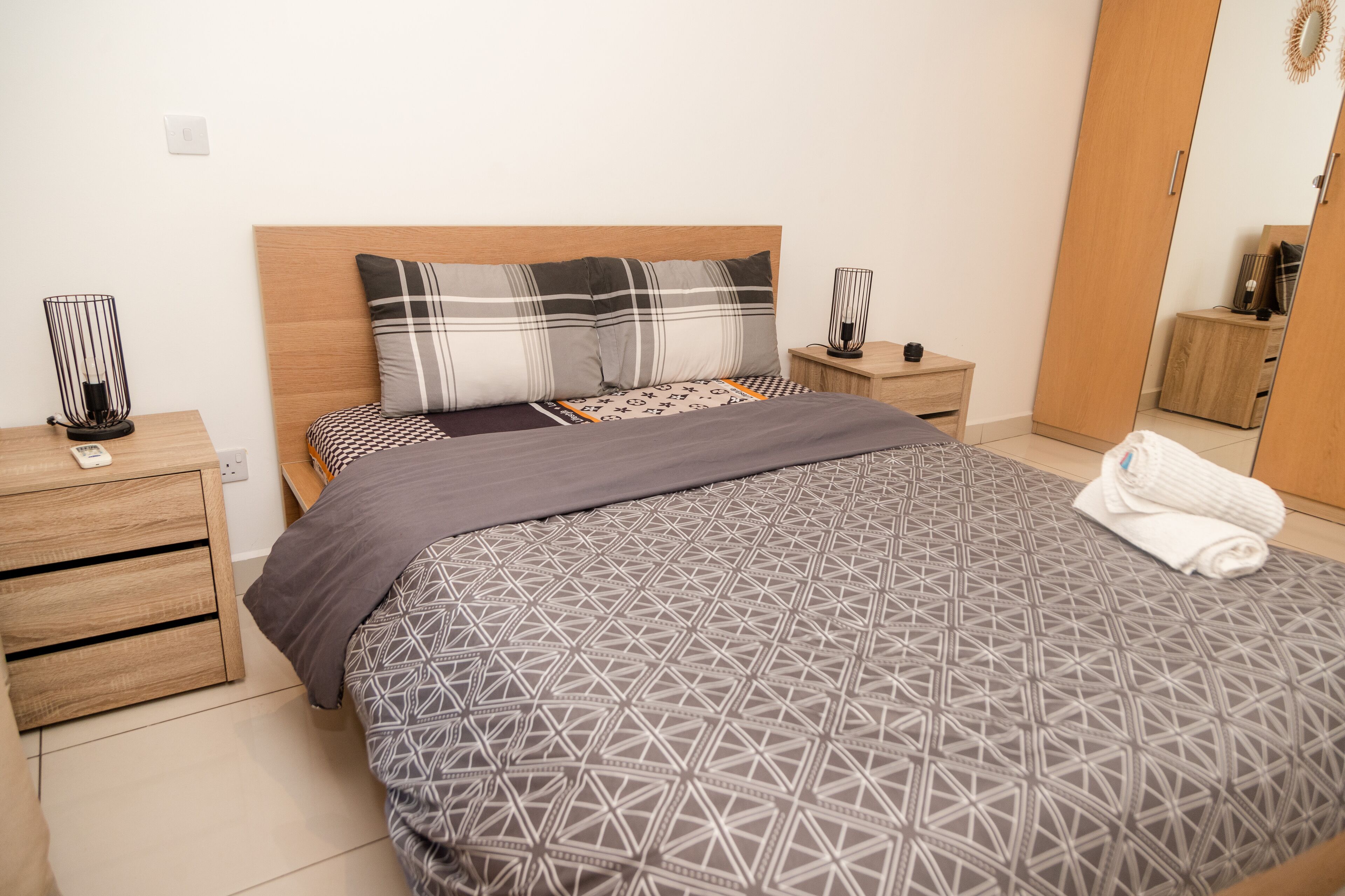 A neatly arranged bedroom with a bed, bedside tables, a wardrobe, and a mirror.