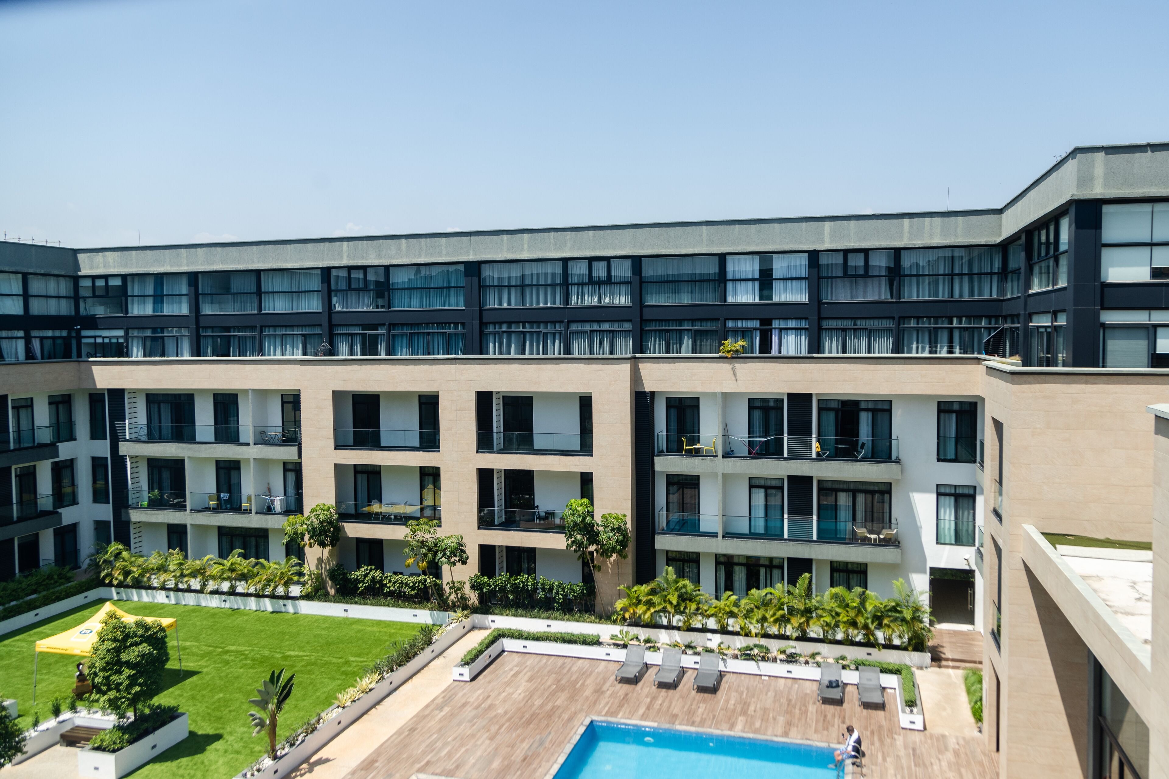 A modern hotel with a pool area, multiple balconies, and a well-maintained garden.