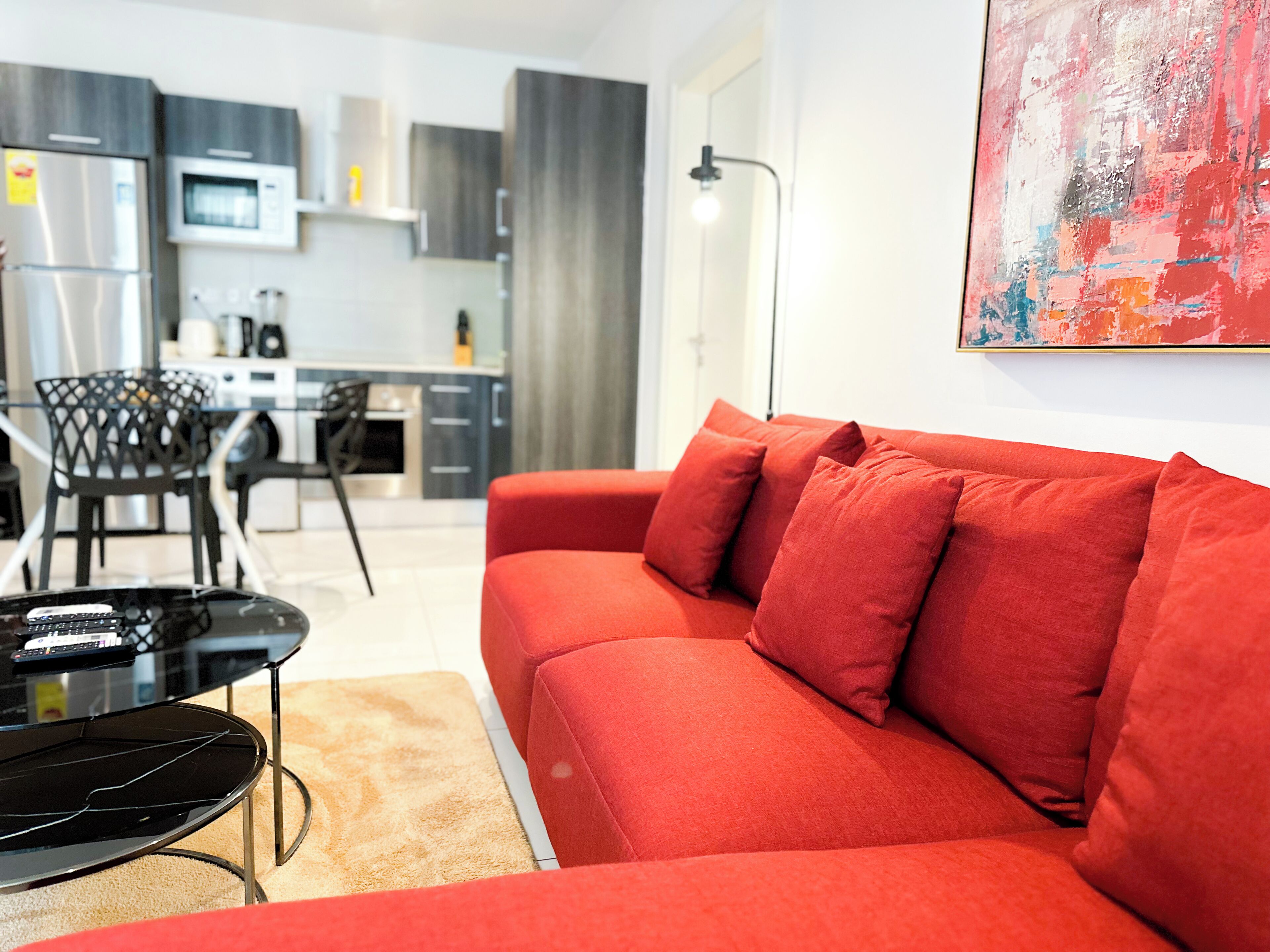Un salon moderne avec un canapé rouge, une table basse noire et une table à manger en verre.