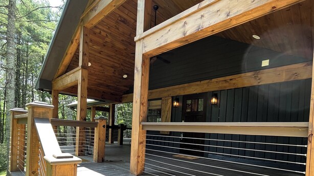A wooden cabin with a covered porch, steps leading to a deck, and a manhole cover at the base.