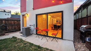 A modern house with a red exterior, a sliding glass door leading to a dining area, and a barbecue grill outside.