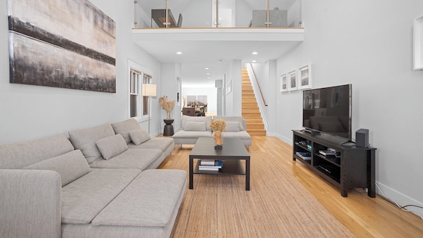 A modern living room with a sectional sofa, a coffee table, a TV, and a staircase leading to an upper level.