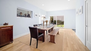 A modern dining room with a wooden table, chairs, and a bench. There are framed pictures on the wall and a window with a view of the outdoors.