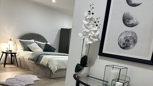 Et moderne soveværelse med seng, sengebord, lampe og et billede af månen i ramme.