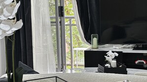 En moderne stue med sofa, sofabord i glas, fjernsyn og en potteplante.