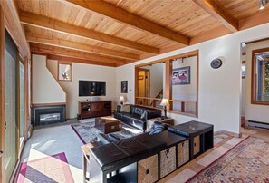 A spacious living room with a fireplace, wooden ceiling beams, a large mirror, and a television. - Free shuttle right to ski lift!  2-BR townhouse, king beds, heated pool, hot tub (Keystone)