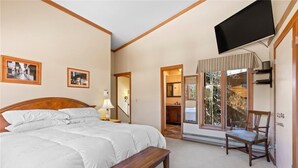 A bedroom with a large bed, a bench, a TV mounted on the wall, and a chair. - One block to Keystone Conference Ctr: 2-BR townhouse, king beds, pool, hot tub (Keystone)