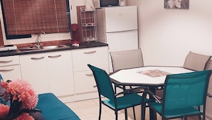 Uma cozinha moderna com forno embutido, uma sala de jantar com mesa e cadeiras redondas, e um sofá com um arranjo floral.