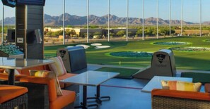 Blick auf einen Golfplatz von einer Lounge mit Sitzgelegenheiten und einem Kontrollturm.