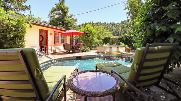 Un jardin avec une piscine, des chaises longues et un parasol rouge.