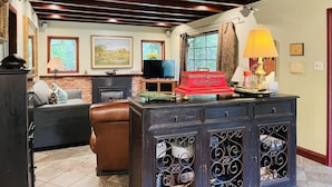 A living room with a fireplace, leather sofa, and a wooden cabinet with decorative metalwork. - Reflections Main House + 3 Cottages w/Baths + Hot Tub, Pool & Dog Friendly (Guerneville)