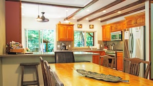 A modern kitchen with wooden cabinets, stainless steel appliances, and a large island with seating. - Reflections Main House + 3 Cottages w/Baths + Hot Tub, Pool & Dog Friendly (Guerneville)