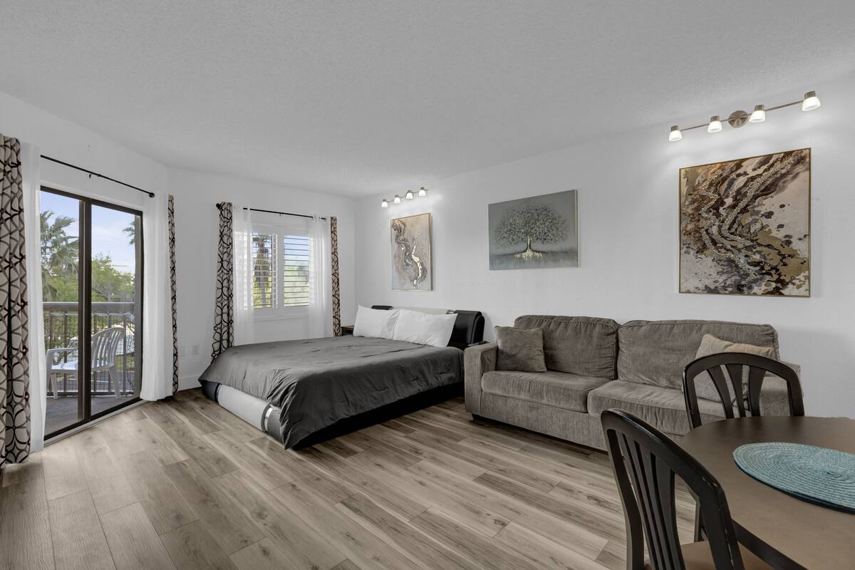 A modern bedroom with a bed, a sofa, a dining table, and artwork on the walls.