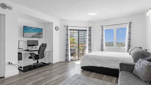 Une chambre moderne avec un lit, un bureau équipé d’un ordinateur et une vue sur le balcon extérieur.