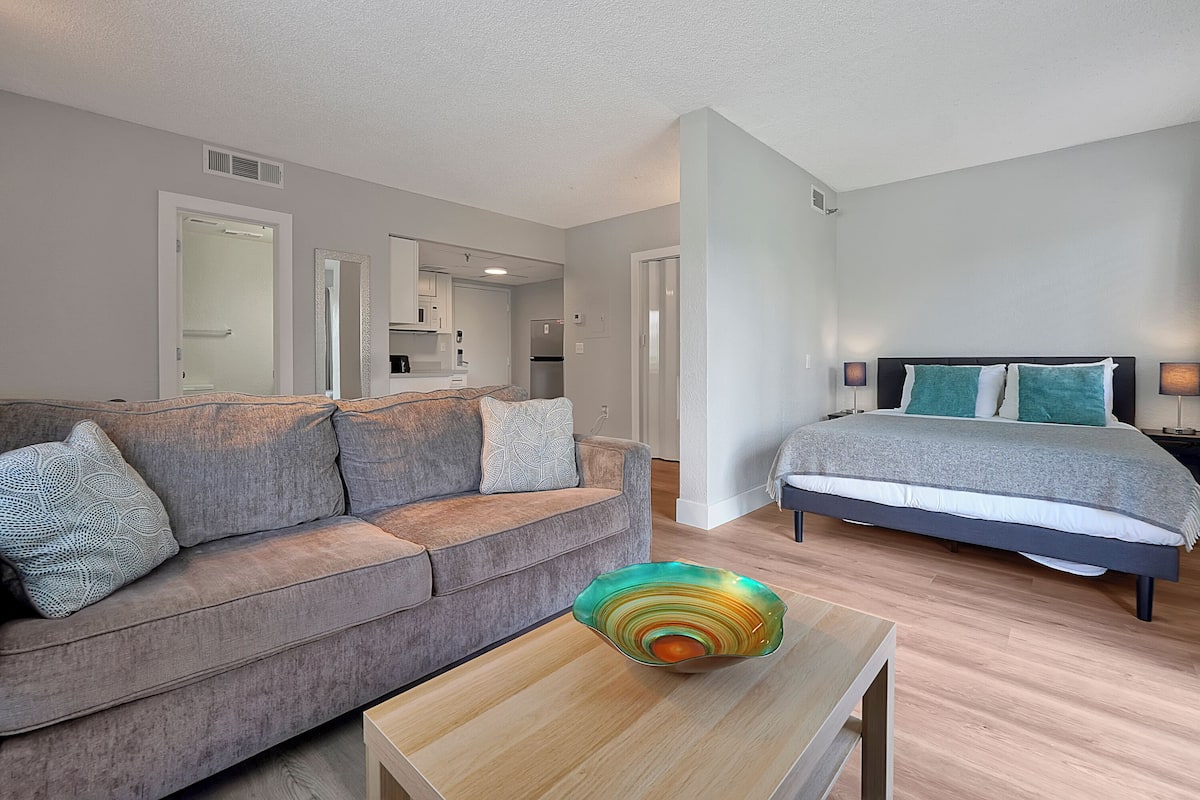 A modern living room with a grey sofa, a coffee table with a decorative bowl, and a bedroom with a bed and nightstands.