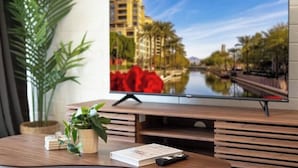Un téléviseur à écran plat posé sur un meuble en bois, avec une télécommande et un livre à côté.
