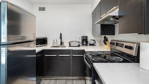 Une cuisine moderne dotée d’appareils électroménagers en acier inoxydable, de meubles de rangement aux couleurs sombres et d’un plan de travail blanc.