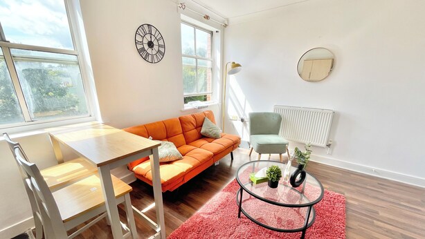A modern living room with a wooden table, orange sofa, and a red rug.