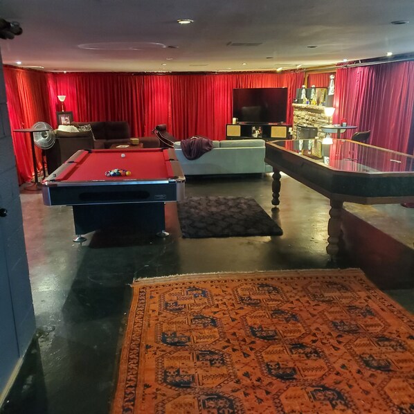 A room with a pool table, a sofa, a television, and a bar area.