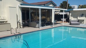 Une piscine dotée d’un patio couvert, de mobilier d’extérieur et surplombant un ciel d’un bleu limpide.
